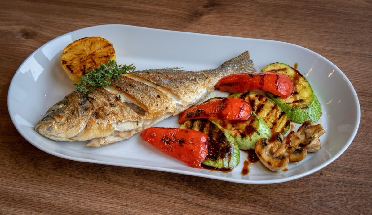 Grilled Danis — Sea Bream in the Tyrian Style — Whole sea bream scored and stuffed with garlic, lemon, and fresh herbs, grilled over charcoal until the skin